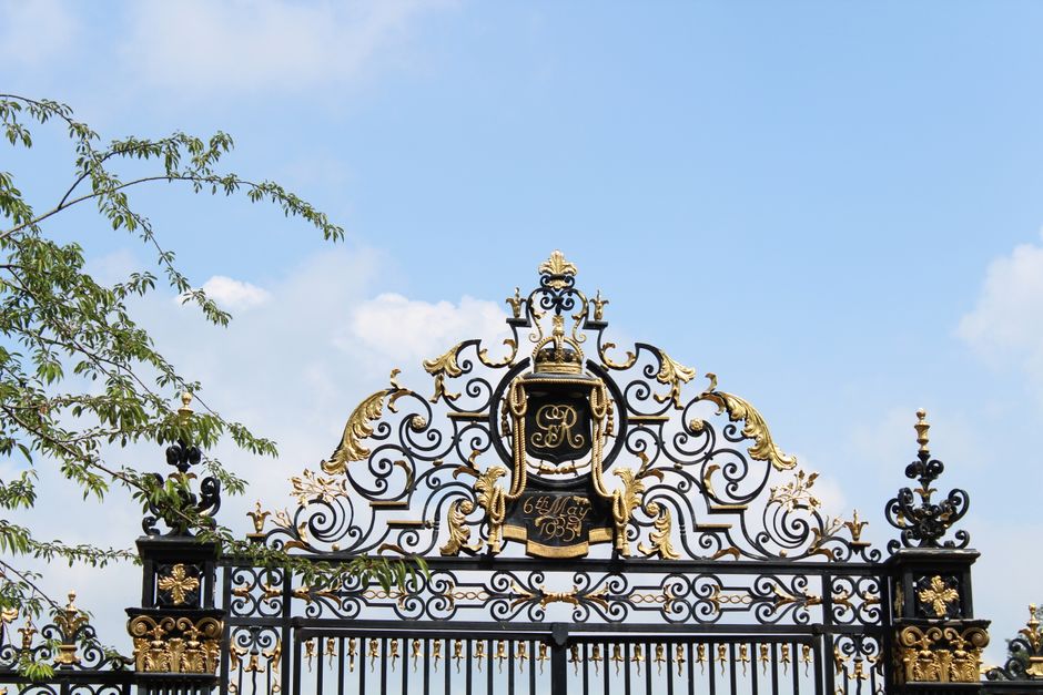 A wrought iron gate with gold accents under a clear sky.